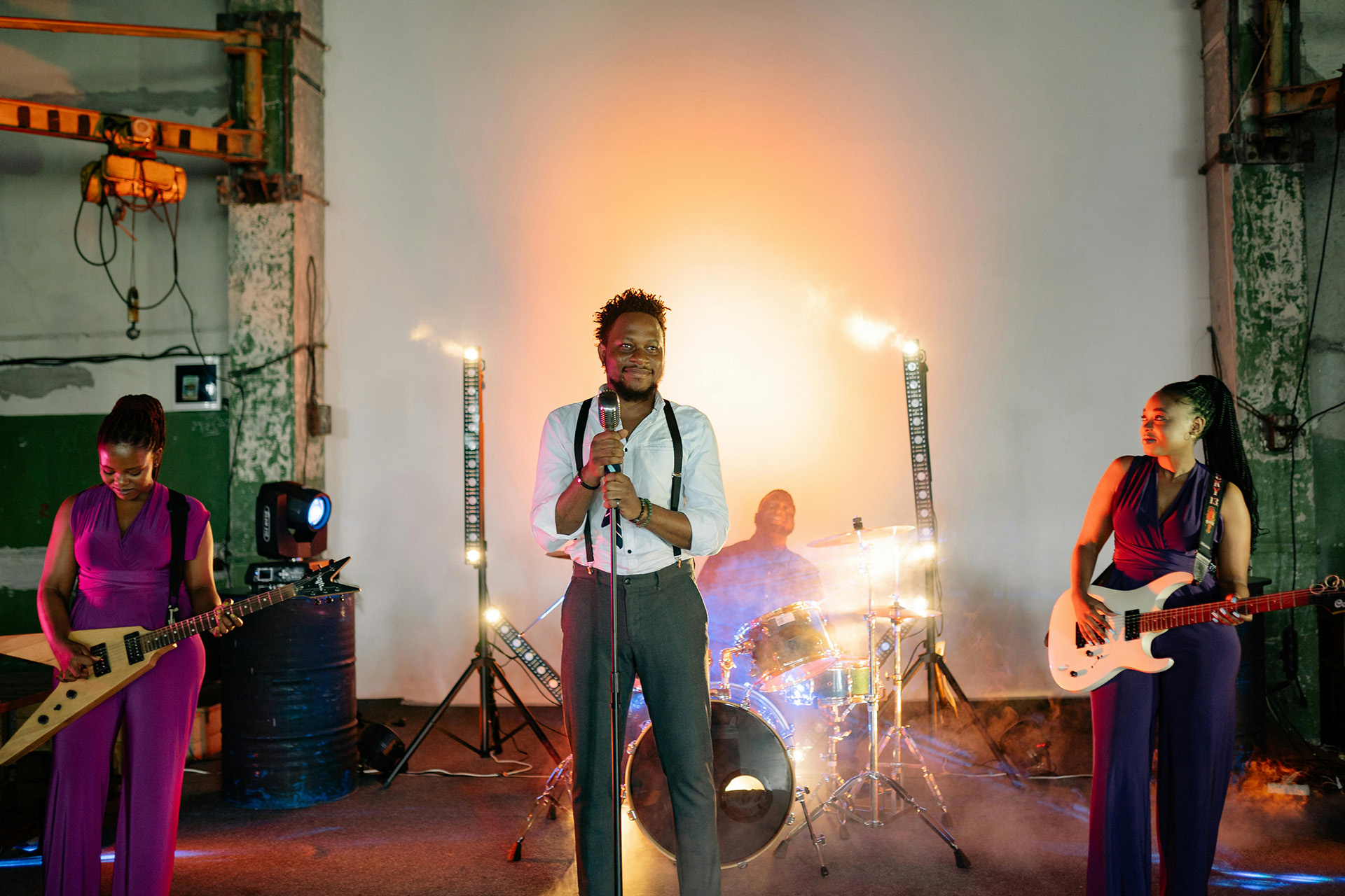 Black audiences support local artists performing live with guitars, drums, and stage lighting in an urban creative venue.